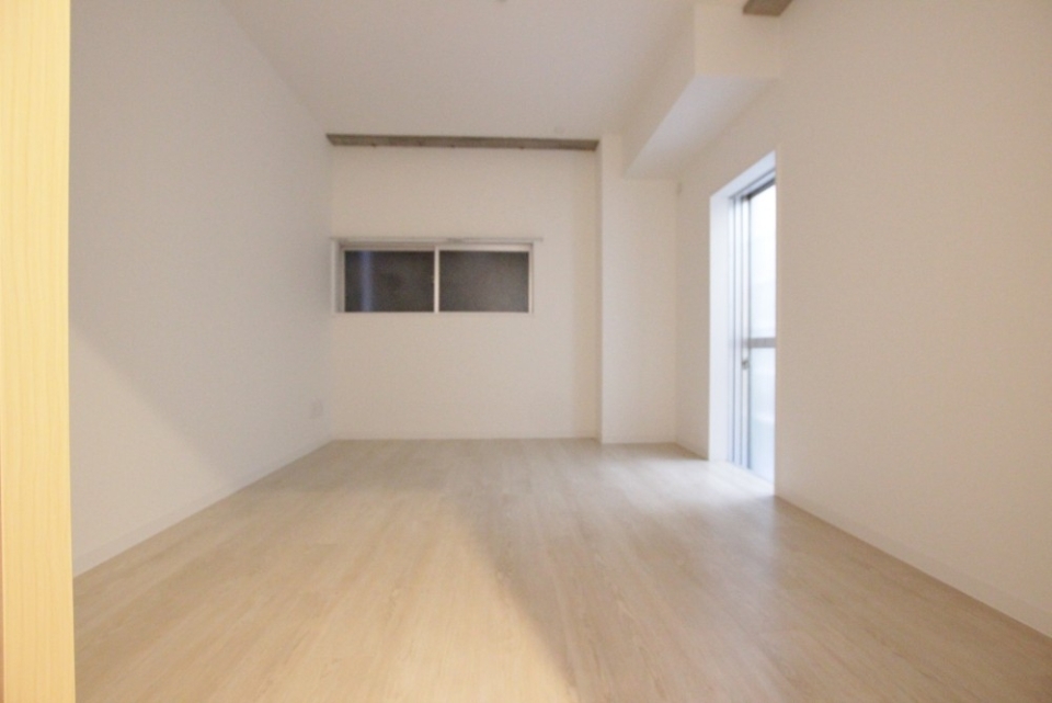 洋室6.8帖。奥の窓の外は隣のビル。明るいドアの向こうはバルコニー。