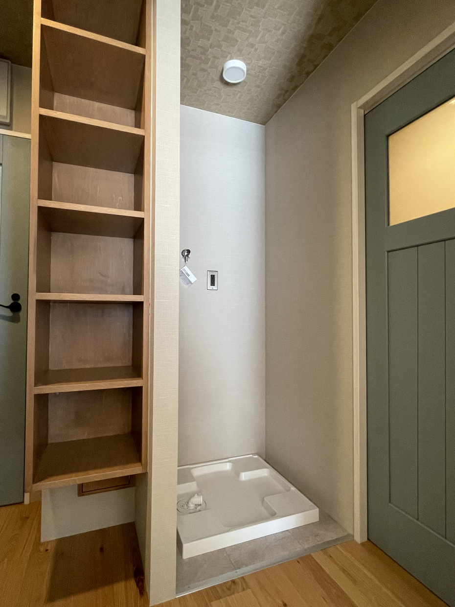 洗濯機置場は廊下に。隣には洗剤などストックできる収納棚