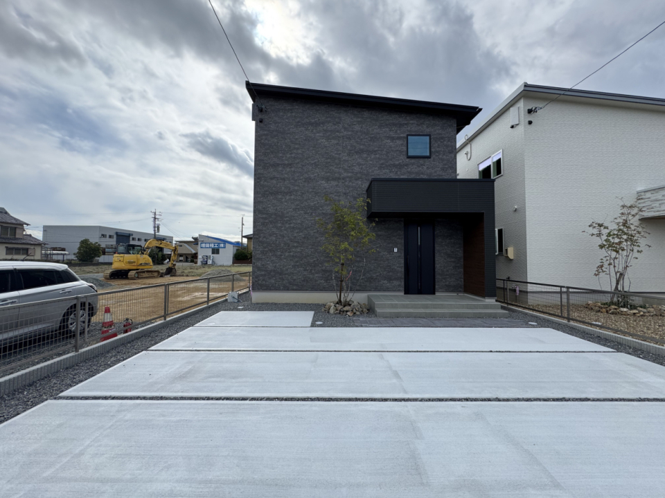 黒い外観とコンクリート打設の駐車場のコントラストが映える